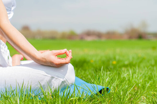 Woman is meditating sitting in Lotus pose on grass at the park. 