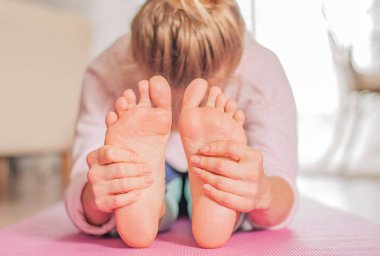 Yoga yapan bir kadın, öne oturmuş eğilmiş poz veriyor, paschimottanasana egzersizi yapıyor.