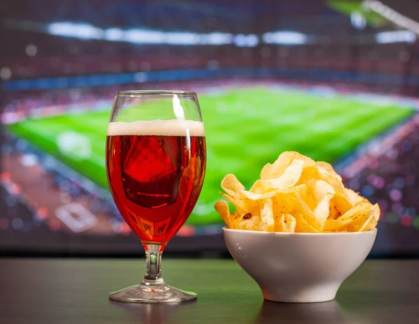 Vasos de cerveza y patatas fritas delante de la televisión, fútbol en casa — Foto de Stock