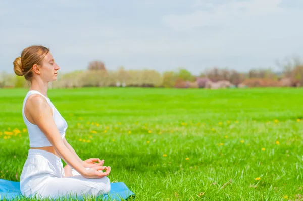 잔디에 연꽃 포즈에 앉아 요가를 연습하는 아름다운 여자 — 스톡 사진