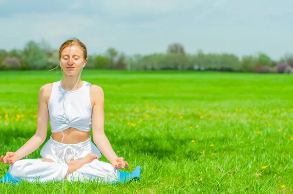 Hermosa mujer está practicando yoga sentada en pose de loto sobre hierba —  Fotos de Stock