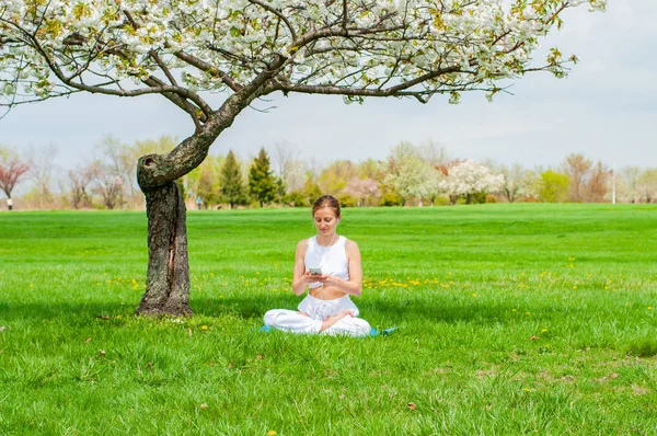 O femeie frumoasă practică yoga stând în Lotus pozând lângă copacul înflorit — Fotografie, imagine de stoc