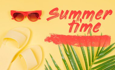 Sarı arka plan, sandalet ve yeşil tropikal palmiye yaprağı ile güneş gözlüğü yaz saati metin.