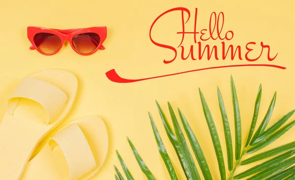 Γεια σας καλοκαίρι κείμενο σε κίτρινο φόντο, σανδάλια και γυαλιά ηλίου με πράσινο τροπικό φύλλο παλάμης. — Φωτογραφία Αρχείου