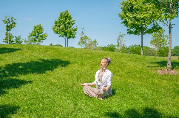 Красивая женщина в стиле бохо с аксессуарами медитирует сидя в позе Лотоса на траве в парке . — стоковое фото