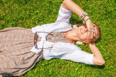 Aksesuarları bir sürü güzel boho tarzı kadın yeşil çim üzerinde yatıyor. Mutlu mometn