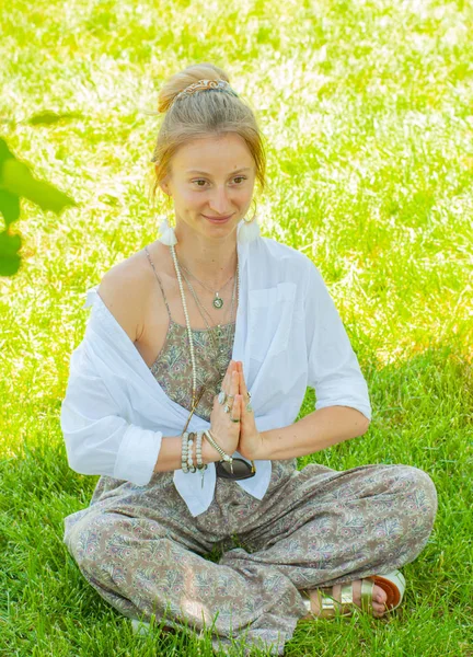 Femeia fericită meditează stând în Lotus pozând pe iarbă. Frumoasă femeie în stil boho cu accesorii care se bucură de o zi însorită în parc . — Fotografie, imagine de stoc