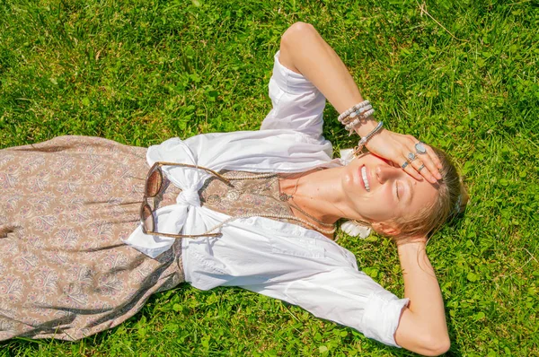 Bella donna in stile boho con un sacco di accessori è sdraiato su erba verde. Mamma felice. — Foto Stock