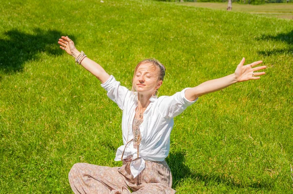 Свобода і щасливий момент. Красива жінка з піднятими руками сидить на траві, насолоджується сонячним днем — стокове фото