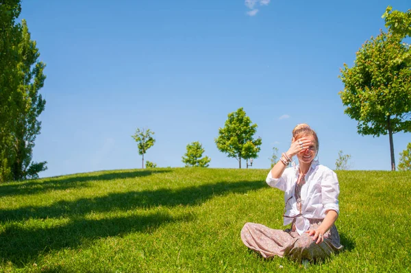 Boldog nő ül a fűben gyep. Gyönyörű boho stílusú nő tartozékokkal élvezze nyári napsütéses nap parkban. — Stock Fotó