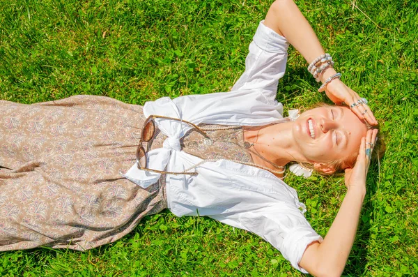 Beautiful boho style woman with a lot of accessories is lying on green grass. Happy mometn Stock Image