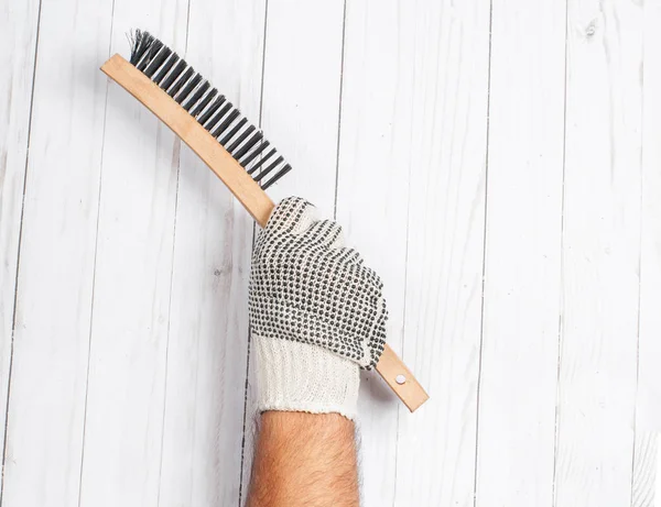 Herramienta. Guante de mano sostiene cepillo de metal de alambre sobre un fondo de madera blanco  . — Foto de Stock