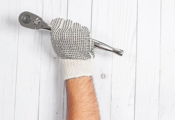Tool. Hand in glove is holding socket wrench on white wooden background .