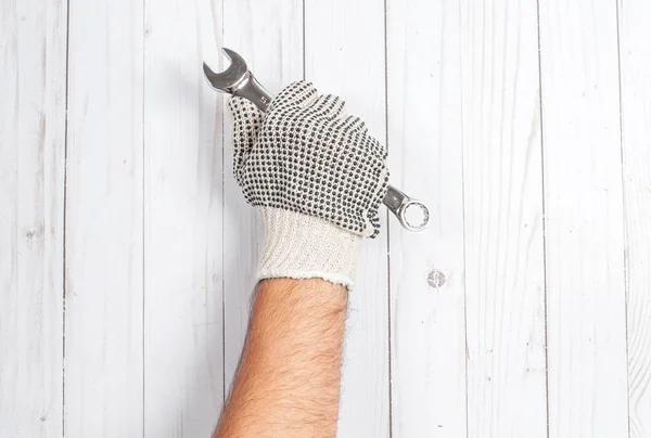 Herramienta. La mano en el guante sostiene la llave inglesa en el fondo blanco de madera . — Foto de Stock