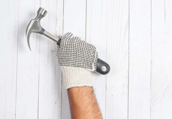 Herramienta. La mano en el guante sostiene el martillo sobre un fondo de madera blanco  . —  Fotos de Stock