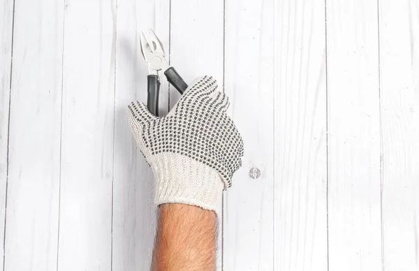 Tool. Hand in glove is holding pliers isolated on wooden background.