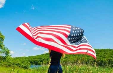 Mavi gökyüzü arka planda Amerikan bayrağı tutan genç kadın. 4 Temmuz