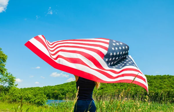 Mujer joven sosteniendo bandera americana sobre fondo azul del cielo. 4 de julio — Foto de Stock