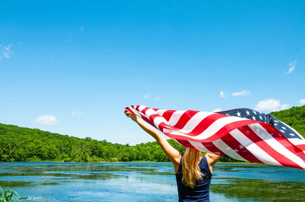 4 de julio. Mujer joven sosteniendo bandera americana en el fondo del lago . — Foto de Stock