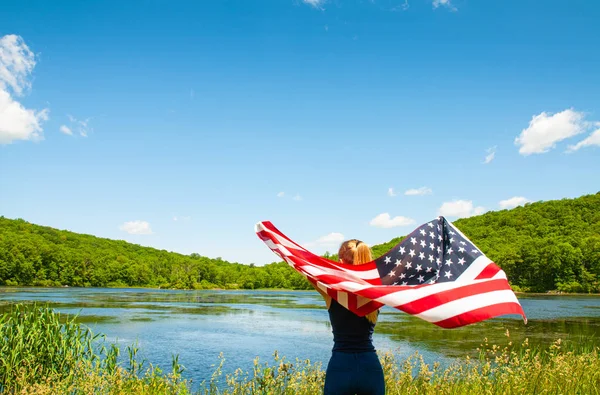 4 de julio. Mujer joven sosteniendo bandera americana en el fondo del lago . — Foto de Stock