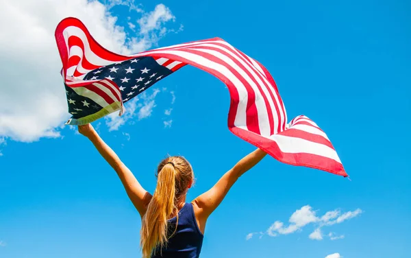 Mujer joven sosteniendo bandera americana sobre fondo azul del cielo . — Foto de Stock