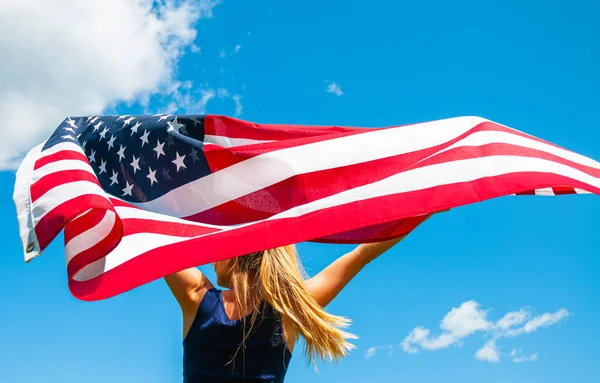 Kobieta trzyma amerykańską flagę na tle błękitnego nieba. Stany Zjednoczone świętować 4 lipca — Zdjęcie stockowe