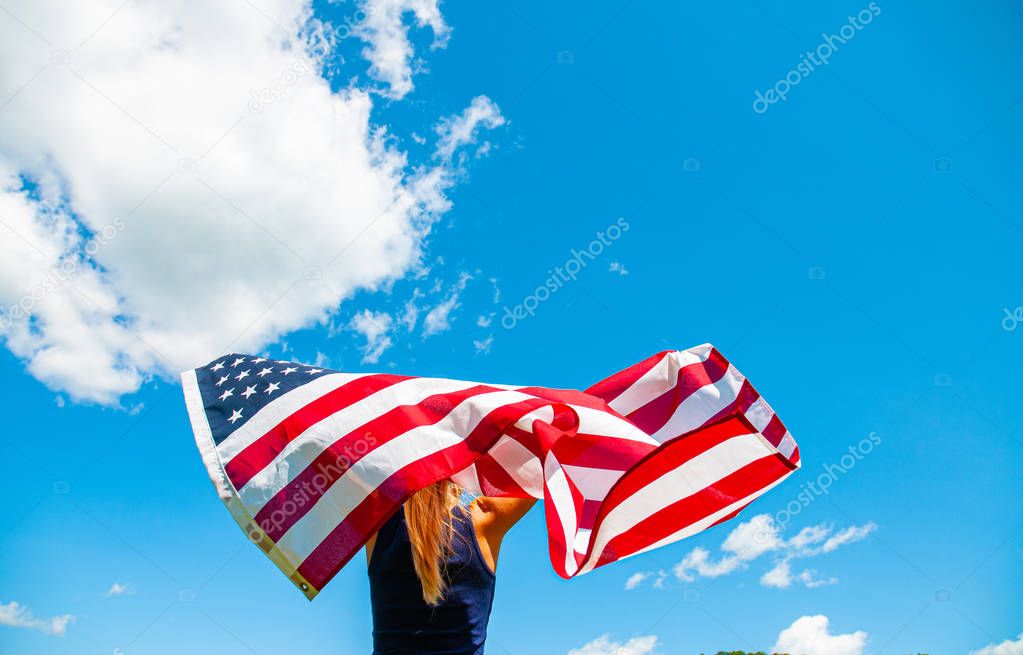 Young woman holding American flag on blue sky background. Independence Day.