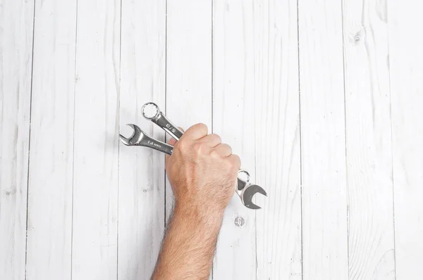 Herramienta. La mano sostiene llaves sobre fondo blanco de madera . —  Fotos de Stock