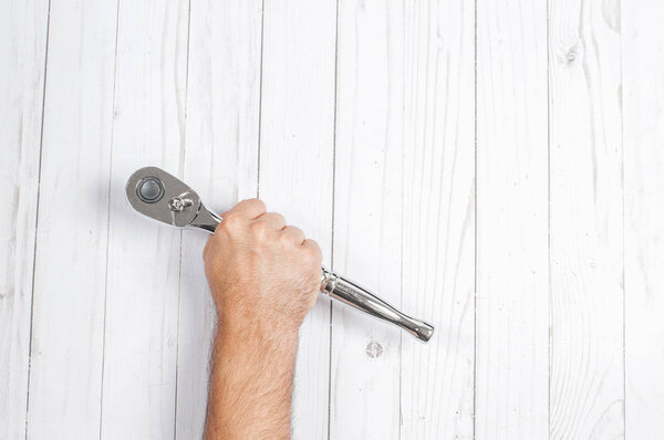 Инструмент. Рука держит гаечный ключ на деревянном фоне
 . 