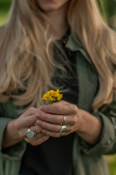 Piękna kobieta z długim włosami trzyma kwiat. Ręce z pierścieniami stylowe akcesoria Boho. Brak fokusu — Zdjęcie stockowe