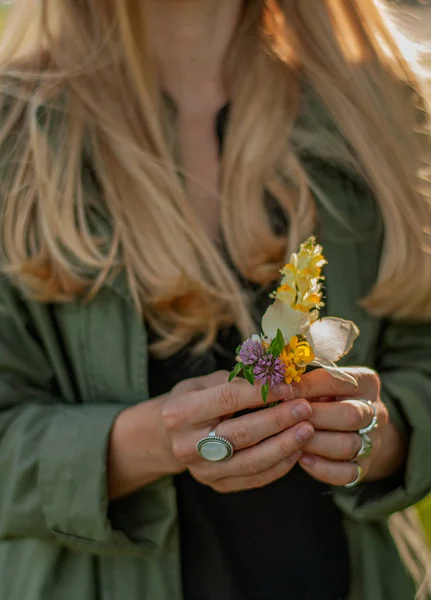 Wanita cantik dengan rambut panjang memegang bunga. Tangan dengan aksesoris boho bergaya cincin. Tidak ada fokus — Stok Foto