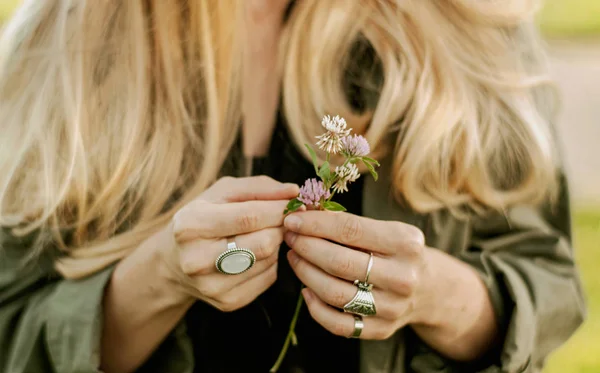 Beautiful woman with long hair holding flower. Hands with rings stylish boho accessories. No focus