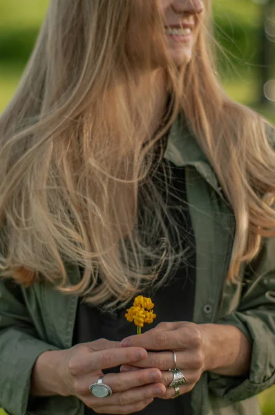 Piękna kobieta z długim włosami trzyma kwiat. Ręce z pierścieniami stylowe akcesoria Boho. Brak fokusu — Zdjęcie stockowe