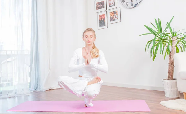Beautiful woman is practicing yoga at home on yoga mat, girl doing Half Lotus Toe Balance pose