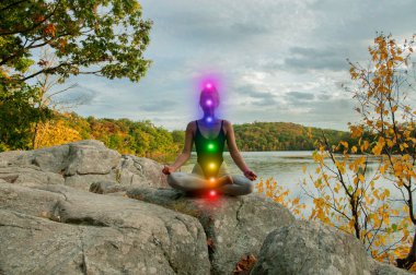 Kadın açık havada parlayan yedi çakra ile meditasyon olduğunu. Kadın gölde yoga yapıyor.