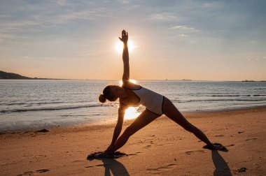 Gün doğumunda sahilde yoga kadının silueti. Kadın deniz kıyısında gün batımında yoga yapıyor.