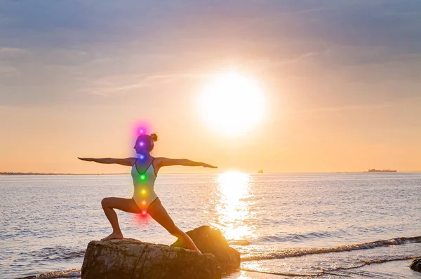 La mujer está meditando con siete chakras brillantes en la playa. Silueta de mujer está practicando yoga al atardecer sobre piedra . —  Fotos de Stock