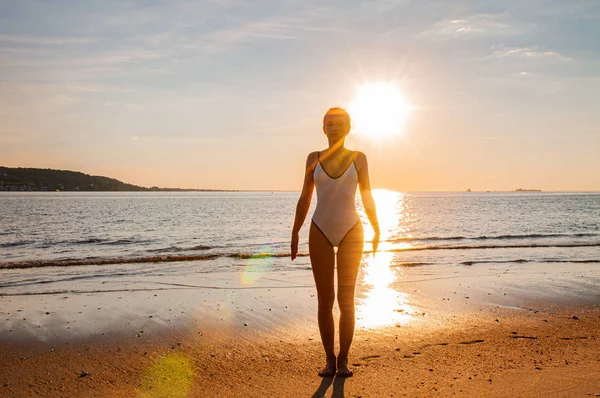Silueta femeie yoga pe plajă la răsărit de soare. Femeia practică yoga la apusul soarelui pe malul mării . — Fotografie, imagine de stoc