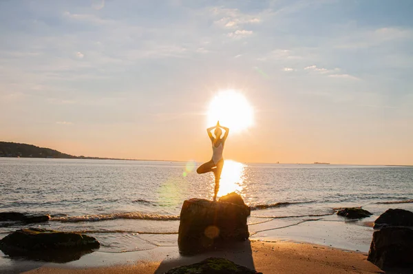 Silueta mujer yoga en la playa al amanecer. Mujer está practicando yoga al atardecer en la orilla del mar . — Foto de Stock