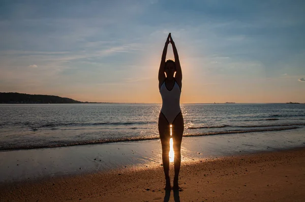 Silhouette Frau Yoga am Strand bei Sonnenuntergang. Frau praktiziert Yoga bei Sonnenuntergang am Meeresufer. — Stockfoto
