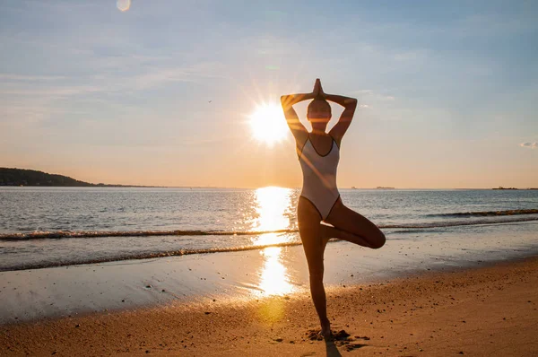 Silhouette Frau Yoga am Strand bei Sonnenaufgang. Frau praktiziert Yoga bei Sonnenuntergang am Meeresufer. — Stockfoto