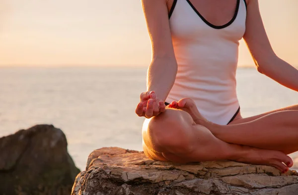 Mulher está praticando ioga sentado em pose de lótus ao nascer do sol. Silhueta de mulher meditando ao pôr do sol na praia — Fotografia de Stock