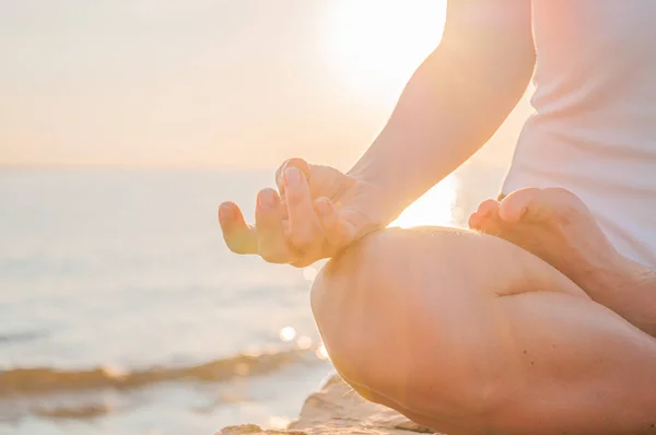 Mulher está praticando ioga sentado em pose de lótus ao nascer do sol. Silhueta de mulher meditando ao pôr do sol na praia — Fotografia de Stock