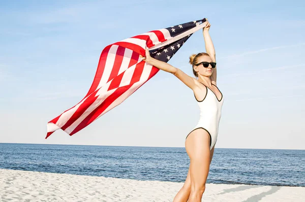 Vacker patriotisk kvinna som innehar en amerikansk flagga på stranden. USA självständighetsdagen, 4 juli. — Stockfoto