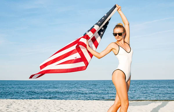 Vacker patriotisk kvinna som innehar en amerikansk flagga på stranden. USA självständighetsdagen, 4 juli. — Stockfoto