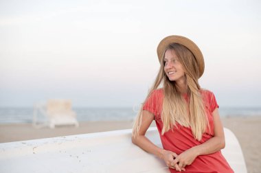 Uzun saçlı güzel kadın ahşap tekne yakınında plajda hasır şapka giymek.