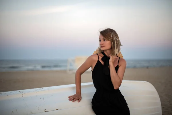 Красива жінка в чорній літній сукні на пляжі біля білого дерев'яного човна . — стокове фото