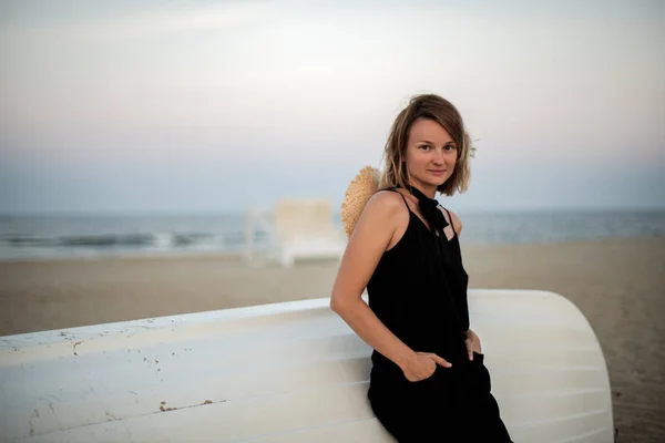 Женщина в черном летнем платье на пляже у белой деревянной лодки . — стоковое фото