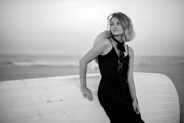 Mulher bonita em vestido de verão preto na praia perto de barco de madeira branca . — Fotografia de Stock