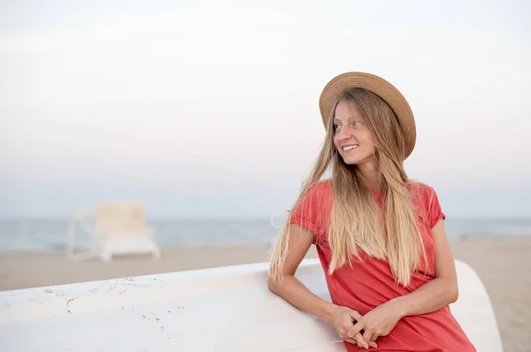 Femeia frumoasă cu păr lung poartă pălărie de paie pe plajă lângă barca de lemn . — Fotografie, imagine de stoc